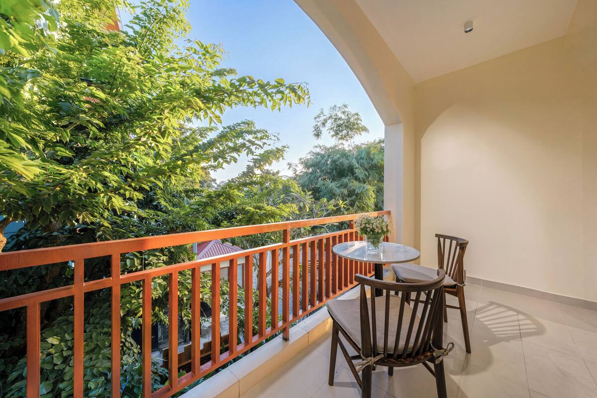 A balcony with a table and chairs, a railing, and a view of greenery.