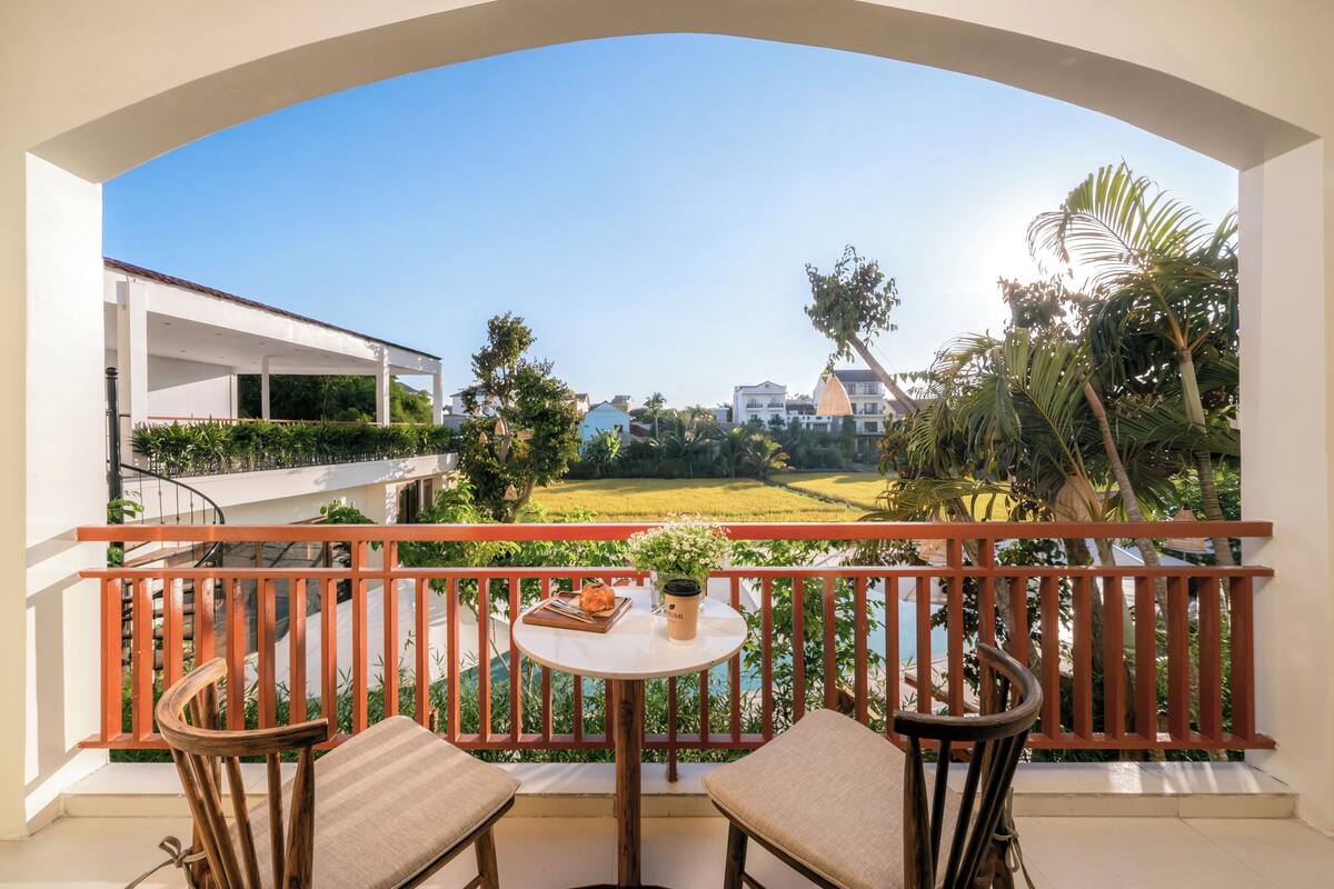A balcony with a table, chairs, and a view of a green landscape and buildings.