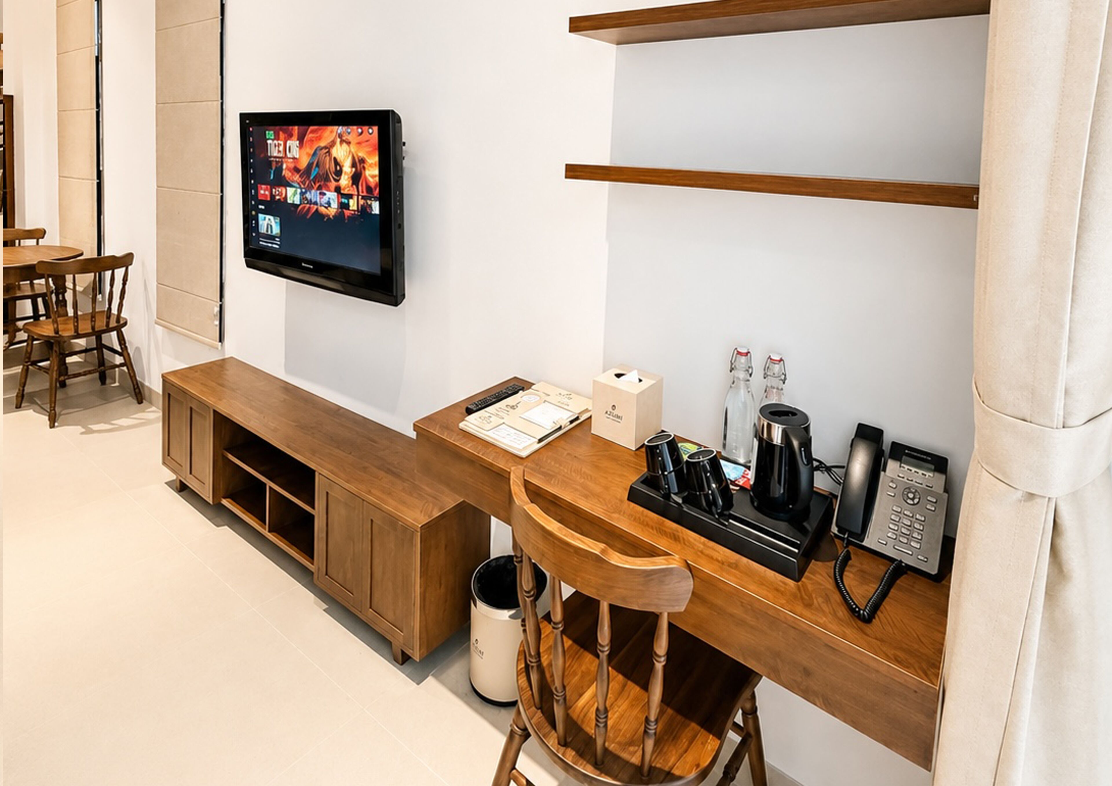 Een hotelkamer met een houten bureau, een aan de muur bevestigde televisie, een telefoon, een koffiezetapparaat en een prullenbak.
