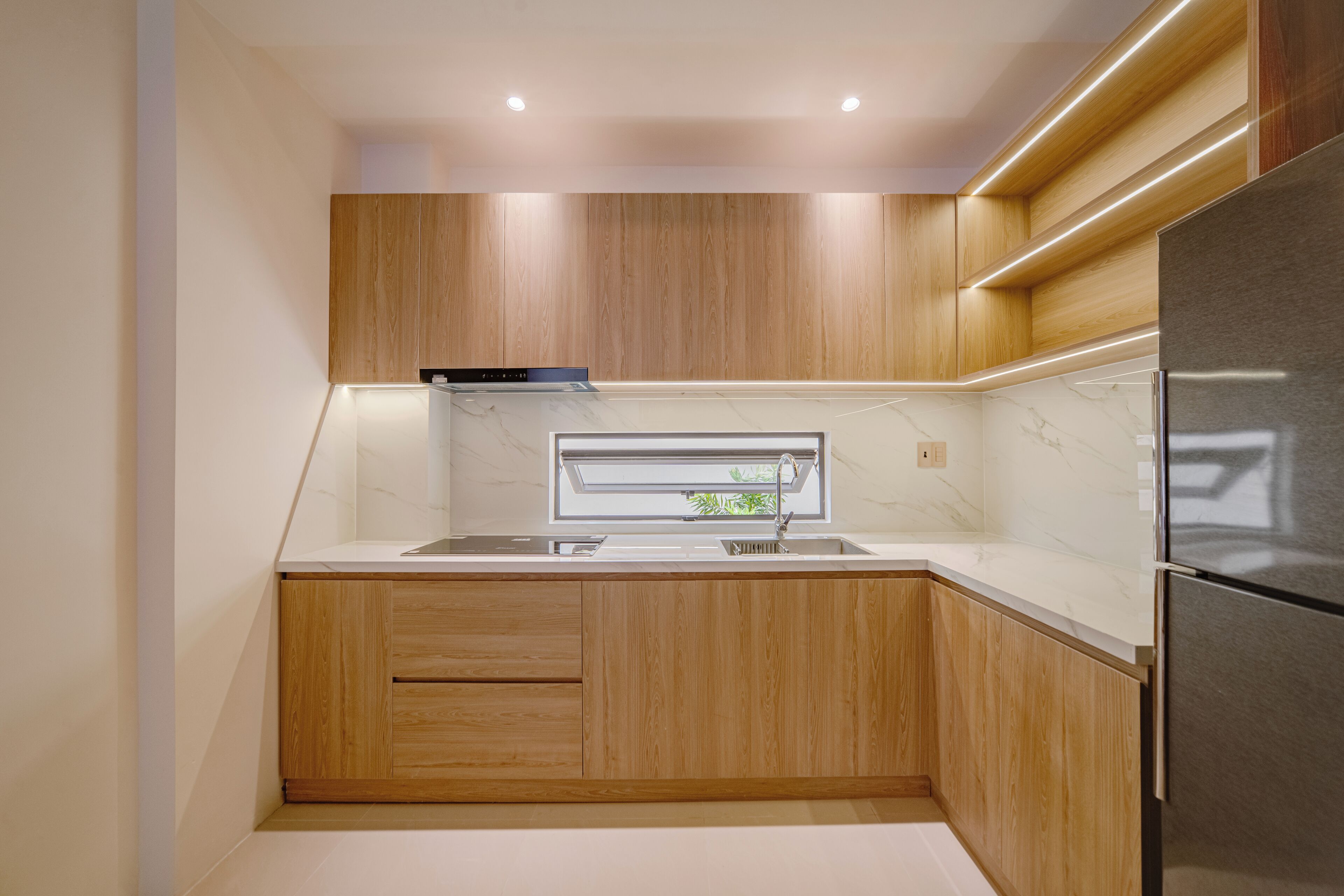 Una cocina compacta con armarios de madera, un refrigerador de acero inoxidable y un ventanal sobre el fregadero.