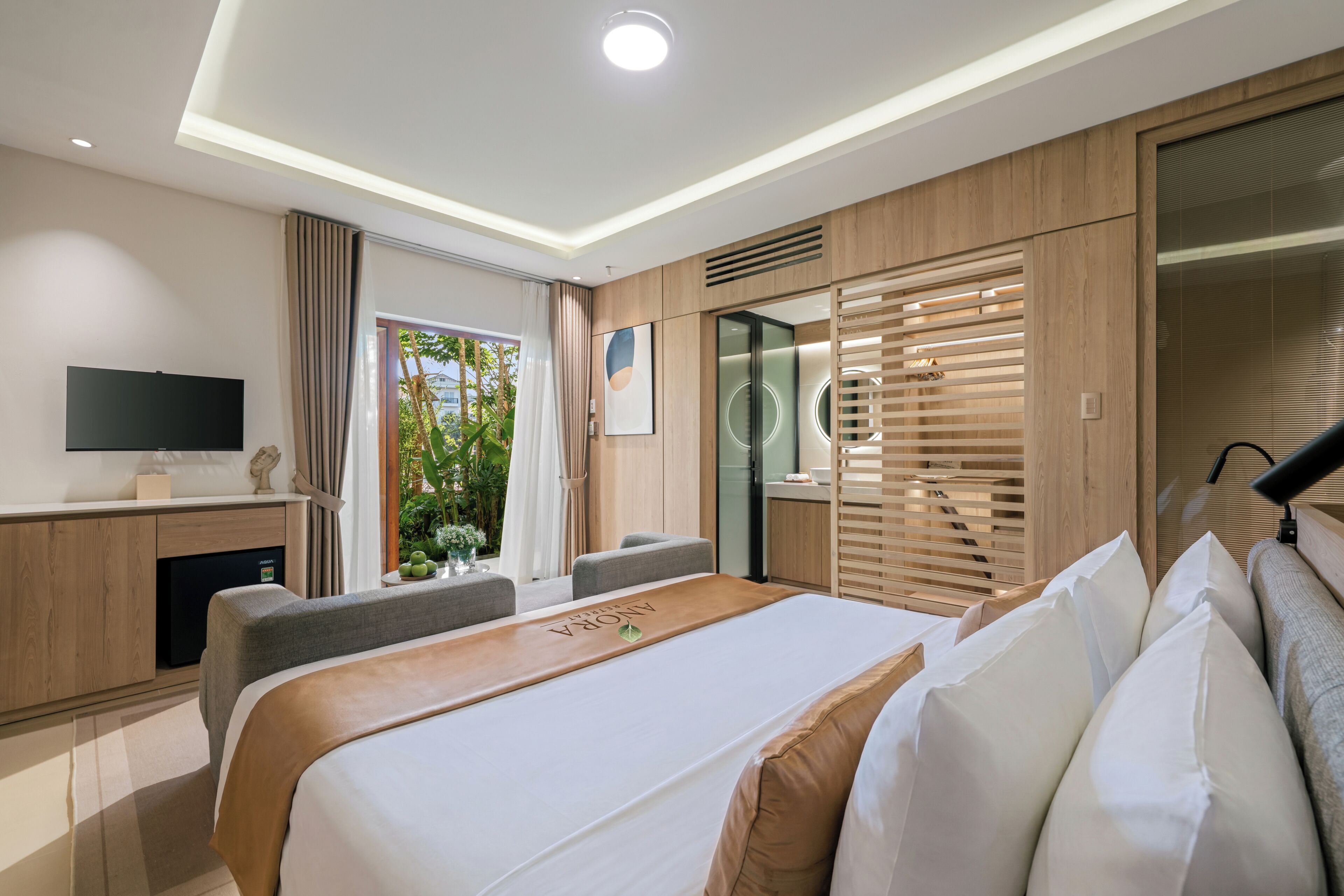 Habitación de hotel moderna con cama, escritorio, televisión y vistas al verde exterior.
