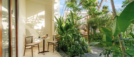 A patio with a table and chairs, surrounded by lush greenery and a stone pathway.