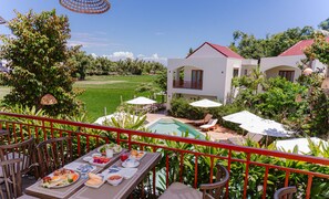 A dining area with a pool view, outdoor seating, and a white building with a red roof. - Anora Retreat Hoi An (Hoi An)
