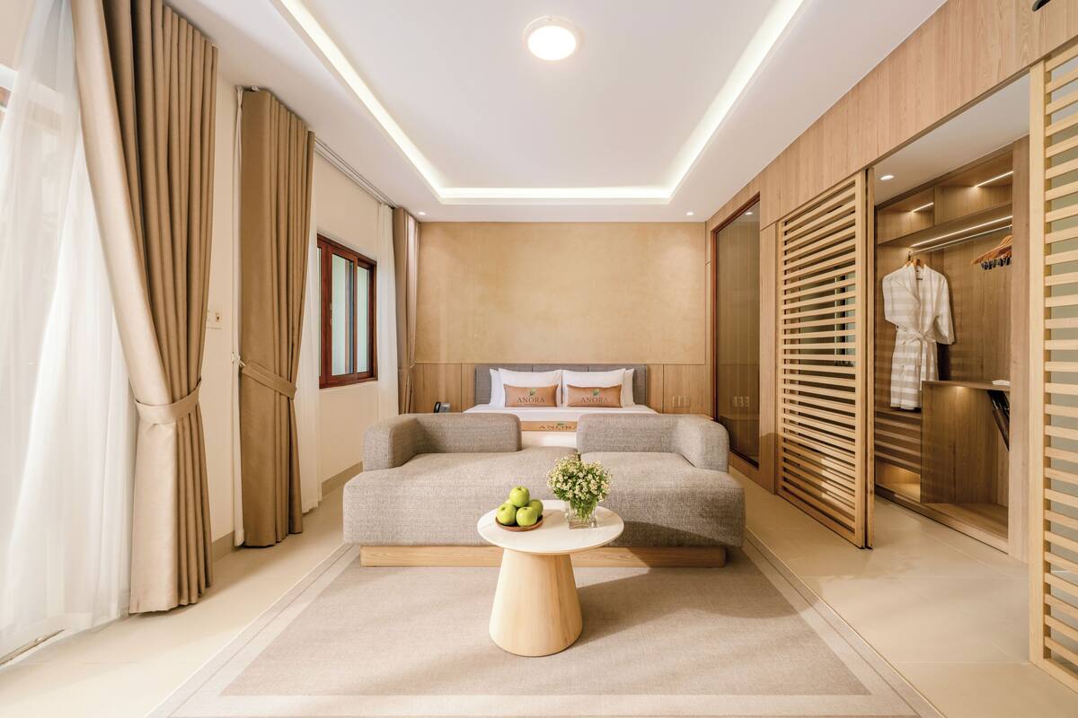 A modern bedroom with a bed, a round wooden table with apples and flowers, and a wardrobe with a hanging robe.