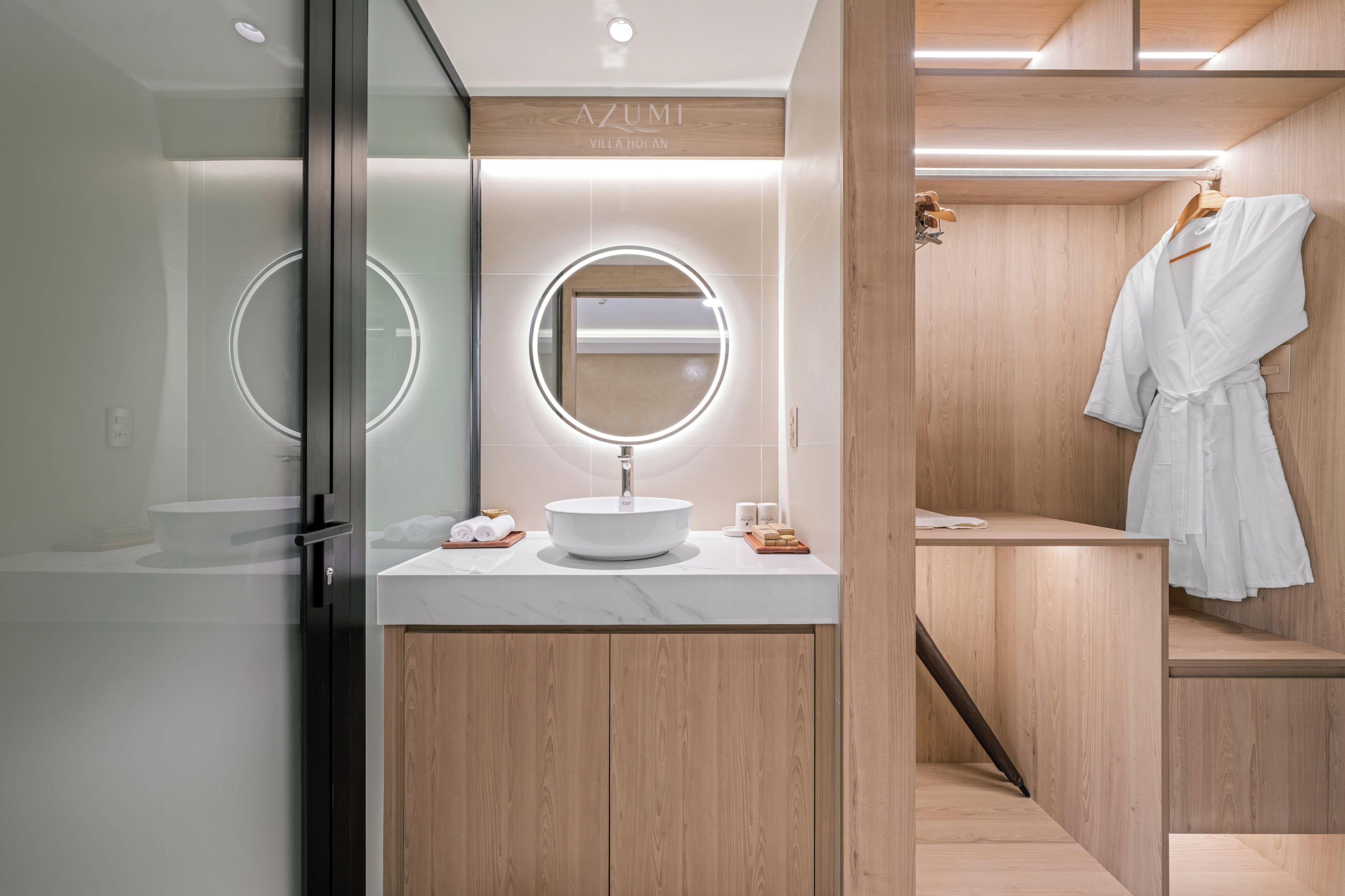 A modern bathroom with a round mirror, a white sink, and a wooden vanity.
