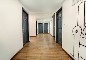 A hallway with wooden flooring, white walls, and doors on both sides. - Collection O Madhavaram Botanical Garden (Chennai)