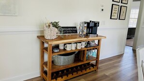 En træ-kaffestation med krus, kaffemaskine og et skilt der står 'Coffee & Wine Bar'.