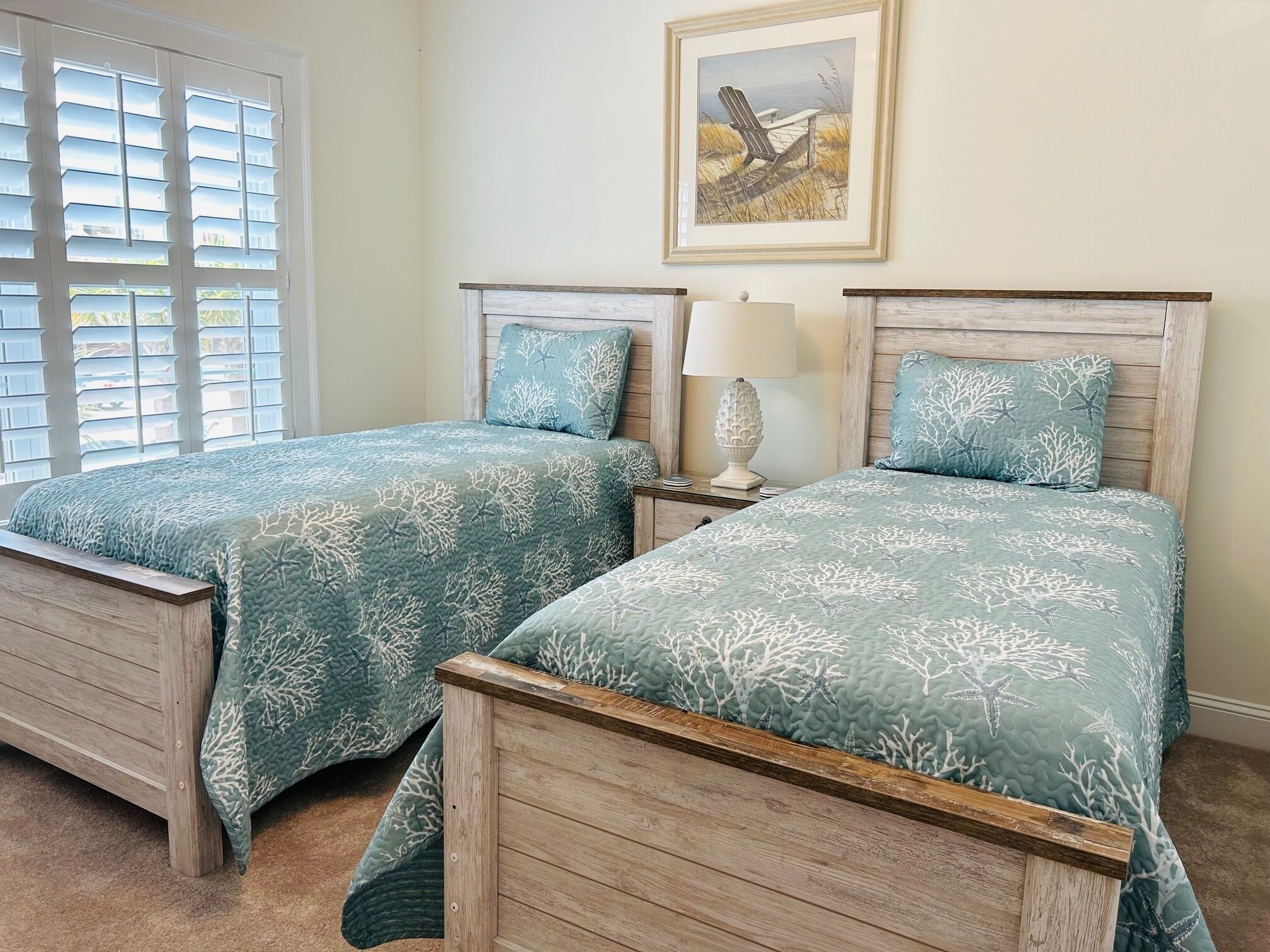 A room with two wooden beds, a window with blinds, a lamp, and a framed picture on the wall.
