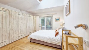 A bedroom with a bed, wooden wardrobe, skylight, window with blinds, bedside table, lamp, and a picture on the wall. - Sleeps 8 guests  in 4 bedrooms (Emsworth)
