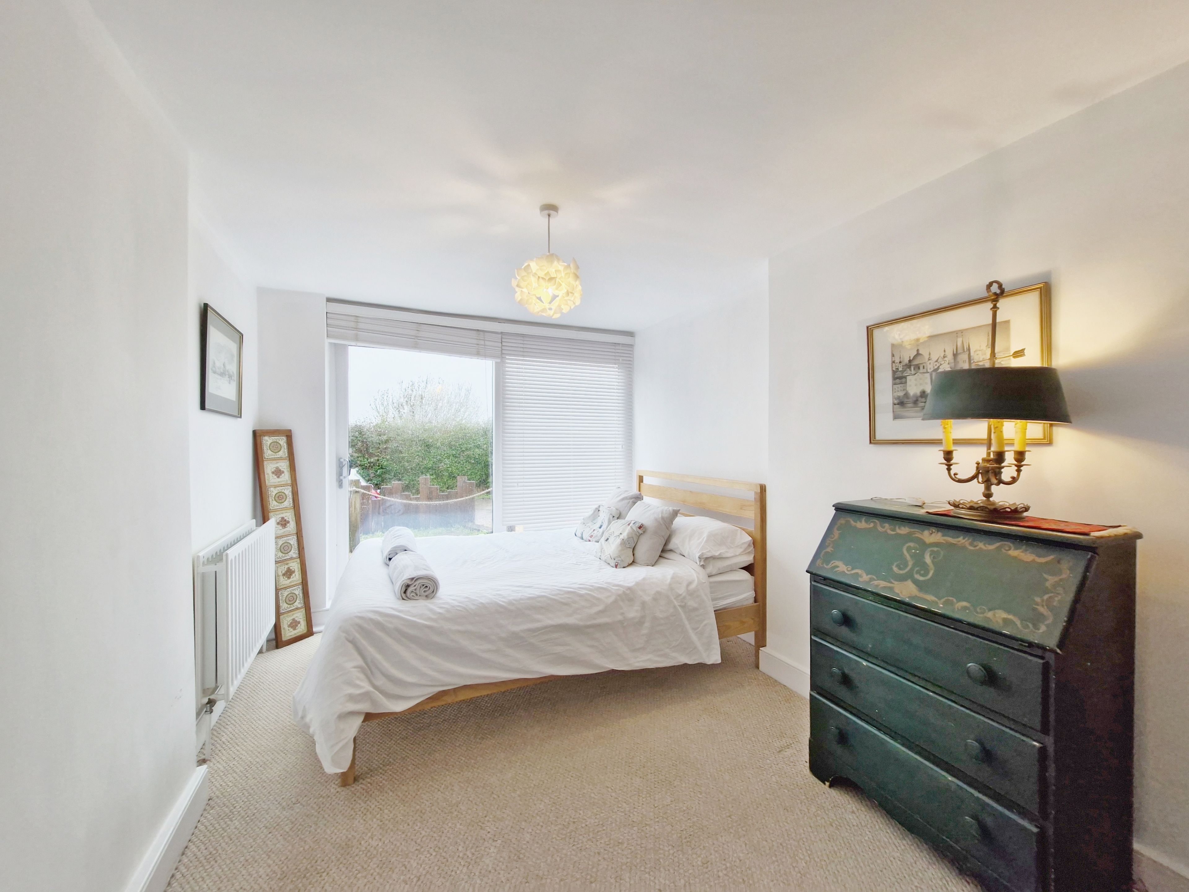 A bedroom with a bed, a dresser, a lamp, and a window.