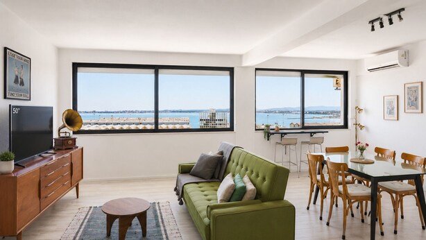 Ein modernes Wohnzimmer mit einem grünen Sofa, einem Fernseher und einem Essbereich mit Tisch und Stühlen.