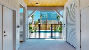 Ein überdachter Außenbereich mit Pool, im Hintergrund ein blaues Haus und ein Metallzaun.
