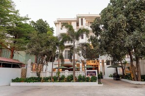 Um hotel com fachada branca, várias varandas e vegetação exuberante.