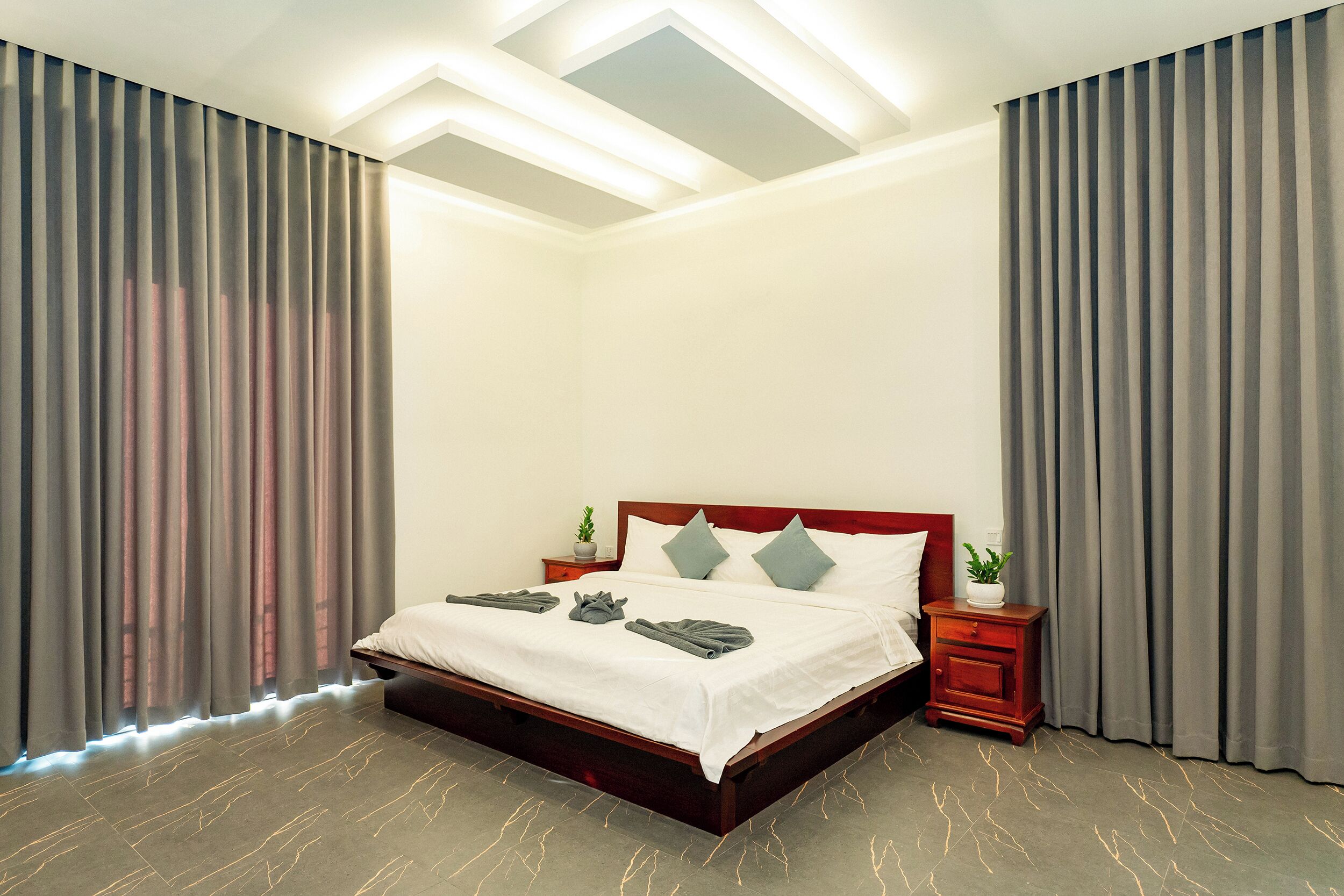 Une chambre à coucher moderne avec un lit en bois, des rideaux gris, une table de chevet avec une plante et un luminaire au plafond.