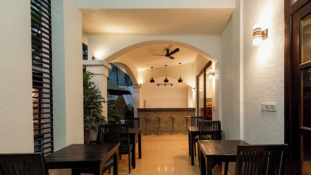 Un restaurante con techo alto, iluminación colgante y una zona central de mesas y sillas.