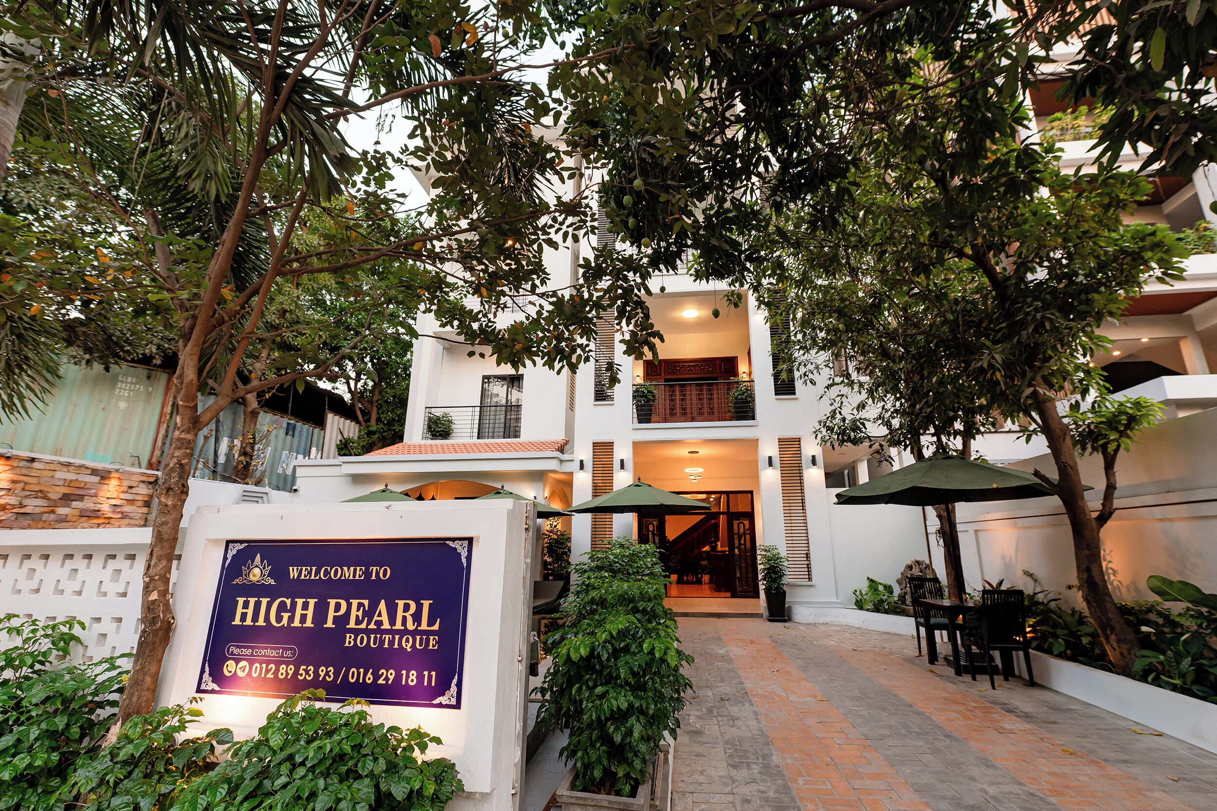Une enseigne indiquant « High Pearl Boutique », avec les numéros de téléphone, une allée pavée, des sièges à l’extérieur et l’entrée du bâtiment.