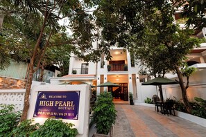 Un letrero que dice 'High Pearl Boutique' con números de contacto, un camino pavimentado, asientos al aire libre y la entrada a un edificio.