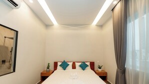 Una habitación de hotel con cama, dos mesitas de noche, una planta en maceta y una ventana con cortinas.