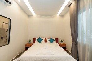 Quarto de hotel com cama, duas mesas de cabeceira, um vaso de planta e janela com cortinas.