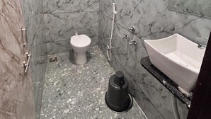 A bathroom with marble walls, a toilet, a sink, and a shower.