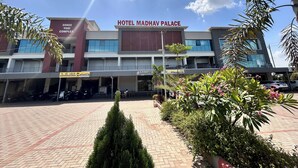 A hotel named 'Hotel Madhav Palace' with a modern architectural style, featuring a prominent entrance, a parking area, and surrounding greenery.