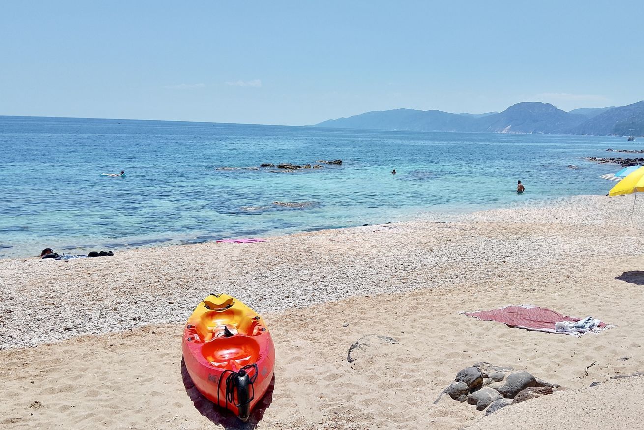 Uma praia com um caiaque, uma toalha e pedras.