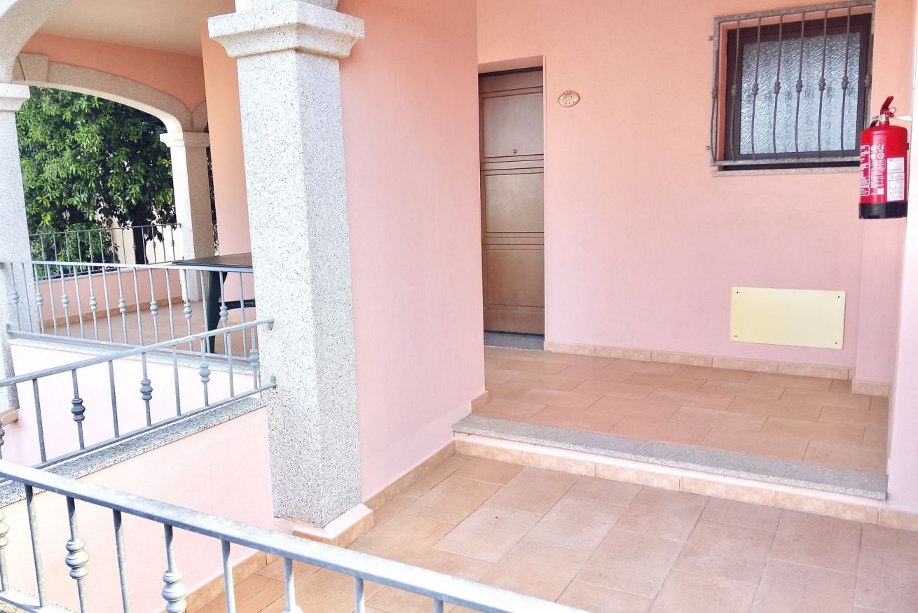 Um edifício com fachada rosa, guarda-corpo de metal na varanda, um extintor fixado na parede e uma porta com janela acima.