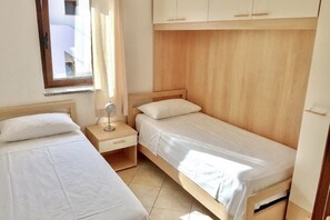 Un dormitorio con dos camas, una mesita de noche, una lámpara y una ventana.