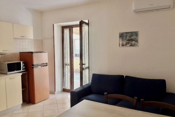 Un espacio habitable compacto con kitchenette, una mesa de comedor, sofá y puerta corrediza de vidrio que da a un área exterior.