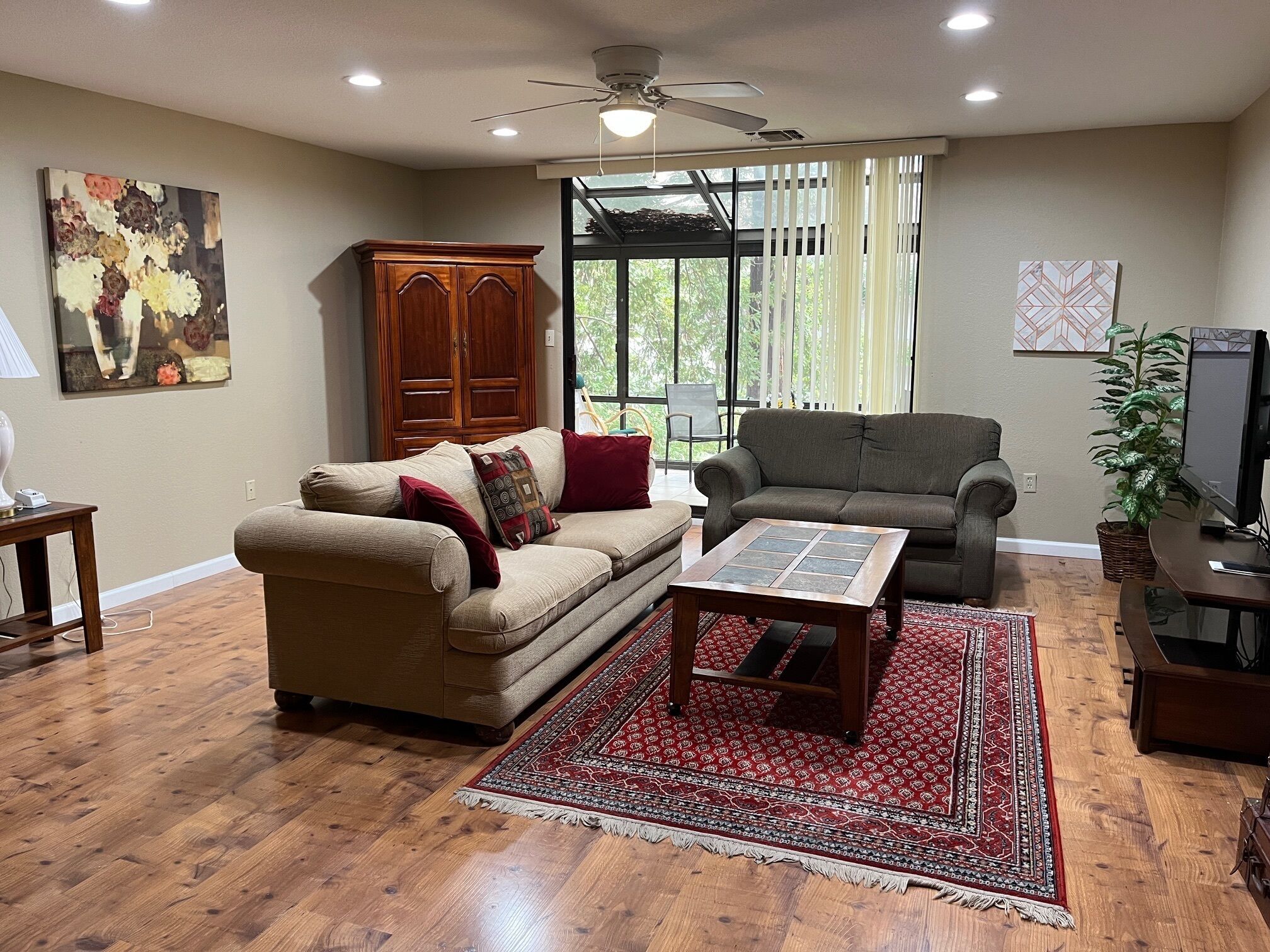 A living room with a wooden floor, two sofas, a coffee table, a TV, and a ceiling fan.