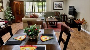 Un área de comedor con una mesa preparada para dos, un sofá, un televisor y una planta.
