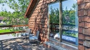 A wooden deck with outdoor furniture, a large window, and a view of trees and a lake. - City Explorer Basecamp Buffalo 1 Bedroom Duplex with AC (Buffalo)