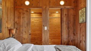 A wooden-paneled room with a bed, a lamp, and a framed picture on the wall. - City Explorer Basecamp Buffalo 1 Bedroom Duplex with AC (Buffalo)