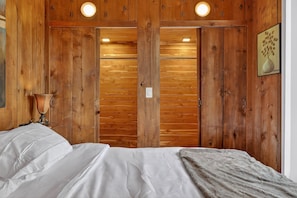 A wooden-paneled room with a bed, a nightstand, a lamp, and a framed picture on the wall. - City Explorer Basecamp Buffalo 1 Bedroom Duplex (Buffalo)