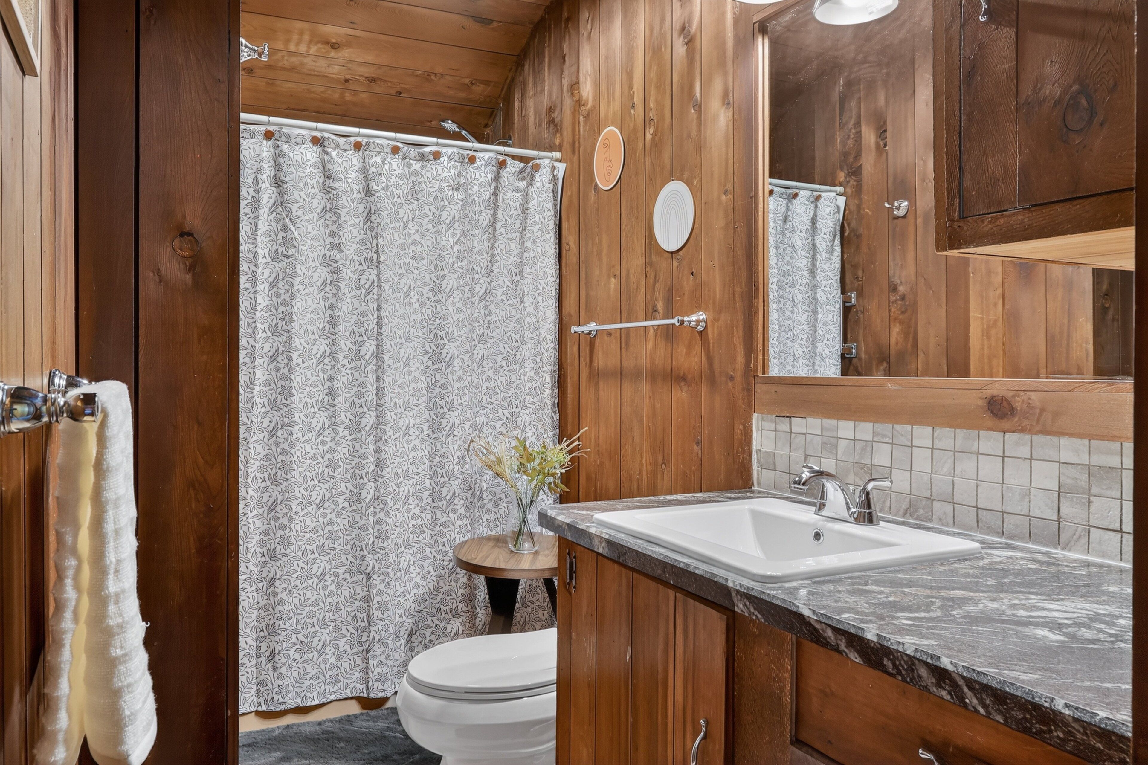 A wooden bathroom with a shower curtain, toilet, sink, and mirror.