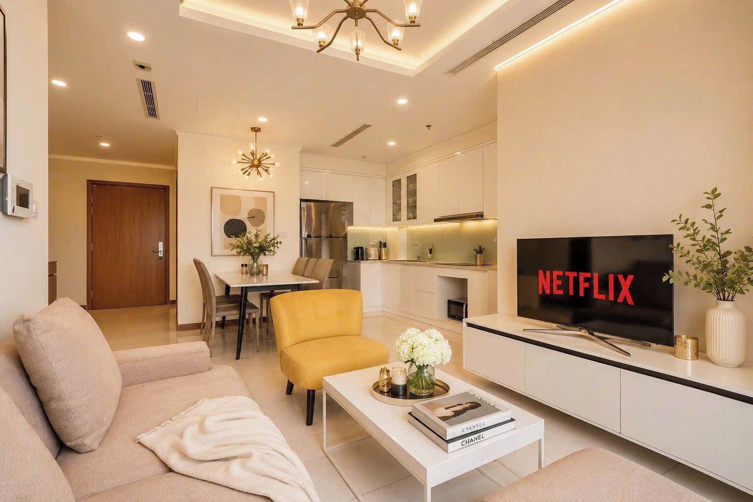 Un salon moderne avec un canapé, un fauteuil jaune, une table basse et un téléviseur affichant le logo de Netflix.