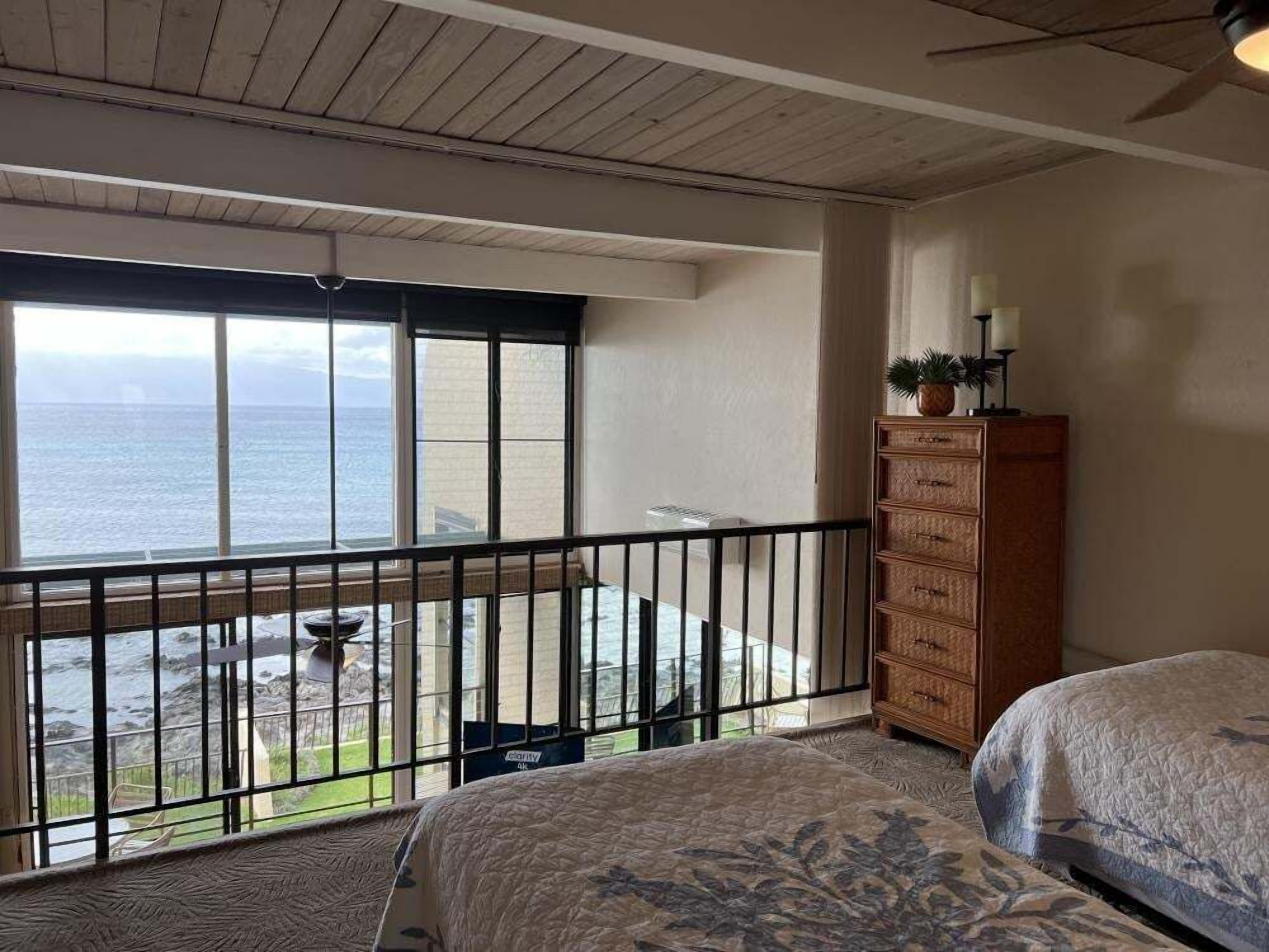 A room with a balcony, a wooden dresser, and a bed with a patterned bedspread.