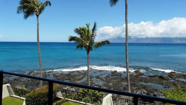 A balcony with a view of the ocean, palm trees, and a rocky shoreline. - Point Oceanfront 2BR Loft with Views - Unit C05 (Lahaina)