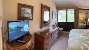 A hotel room with a bed, a television, a dresser, a mirror, and a window. - Point Oceanfront 2BR Loft with Views - Unit C05 (Lahaina)
