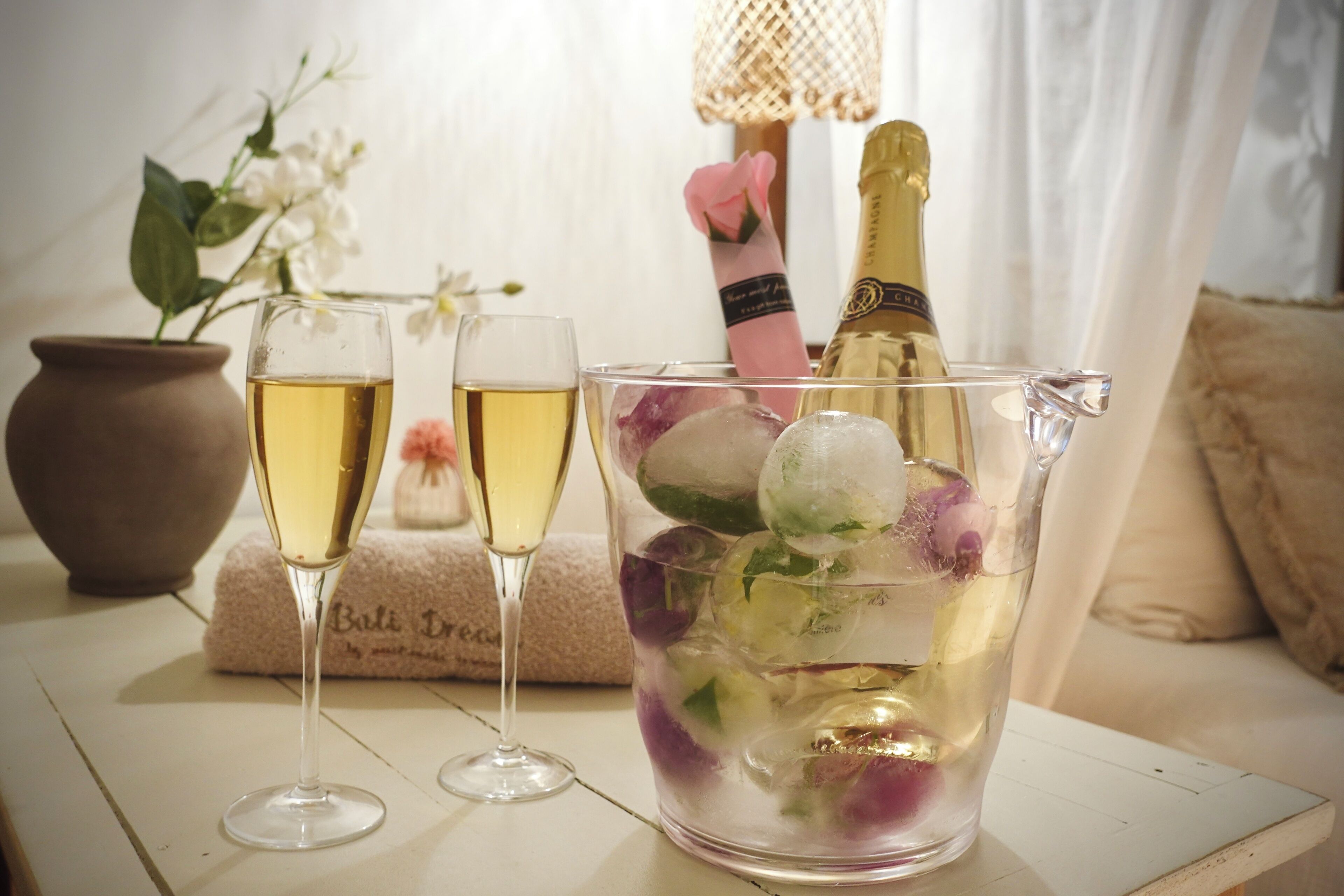 Two glasses of a clear beverage, a bottle of champagne, and a pitcher with ice and fruit.