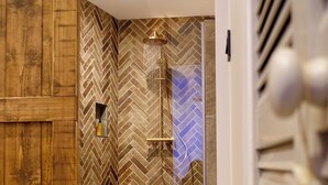 A modern bathroom with a herringbone tile pattern, a glass shower enclosure, and a wooden door. - Unique, romantic luxury suite in Bali with a jacuzzi, near the train station and close to the mountains (Grenoble)