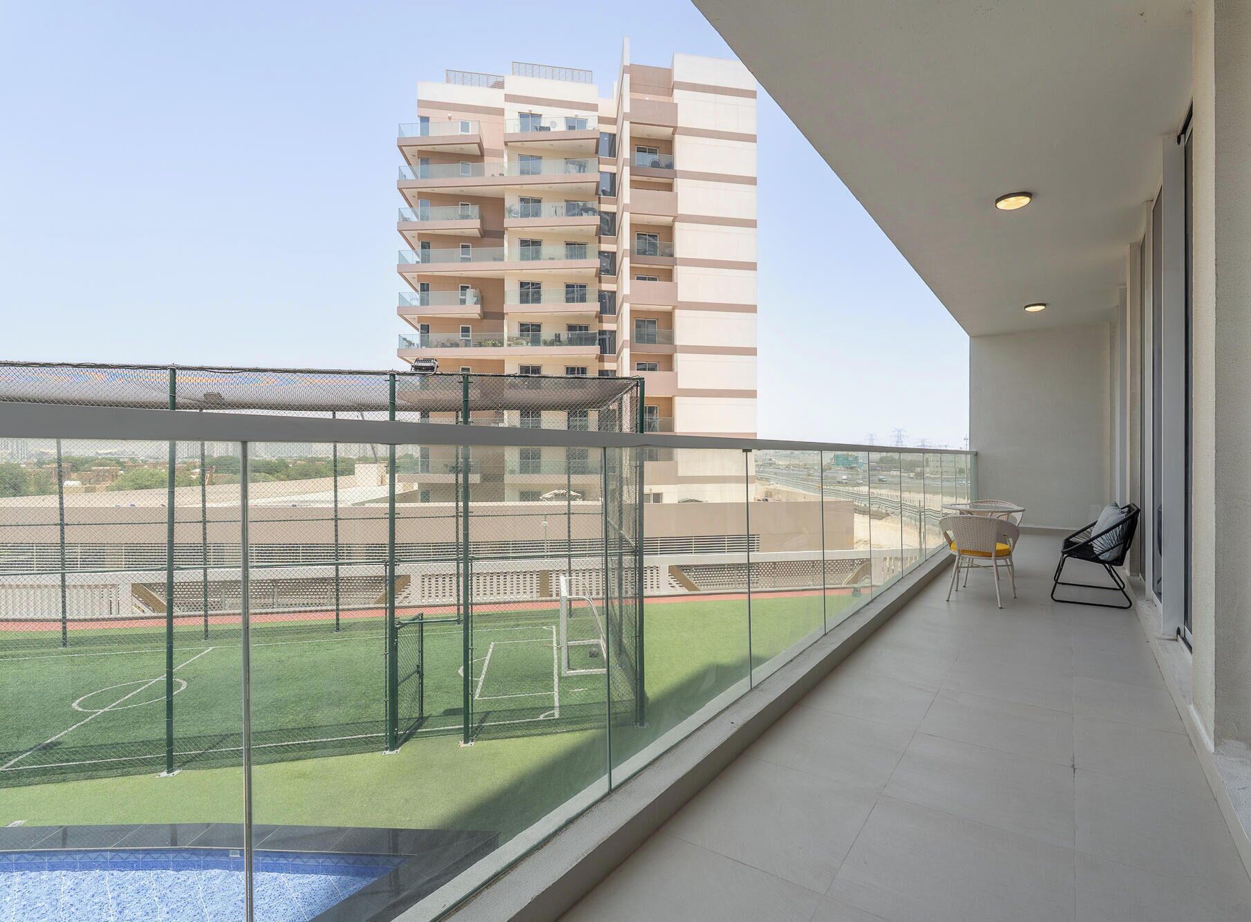 A balcony with a view of a sports field and a tall building in the background.
