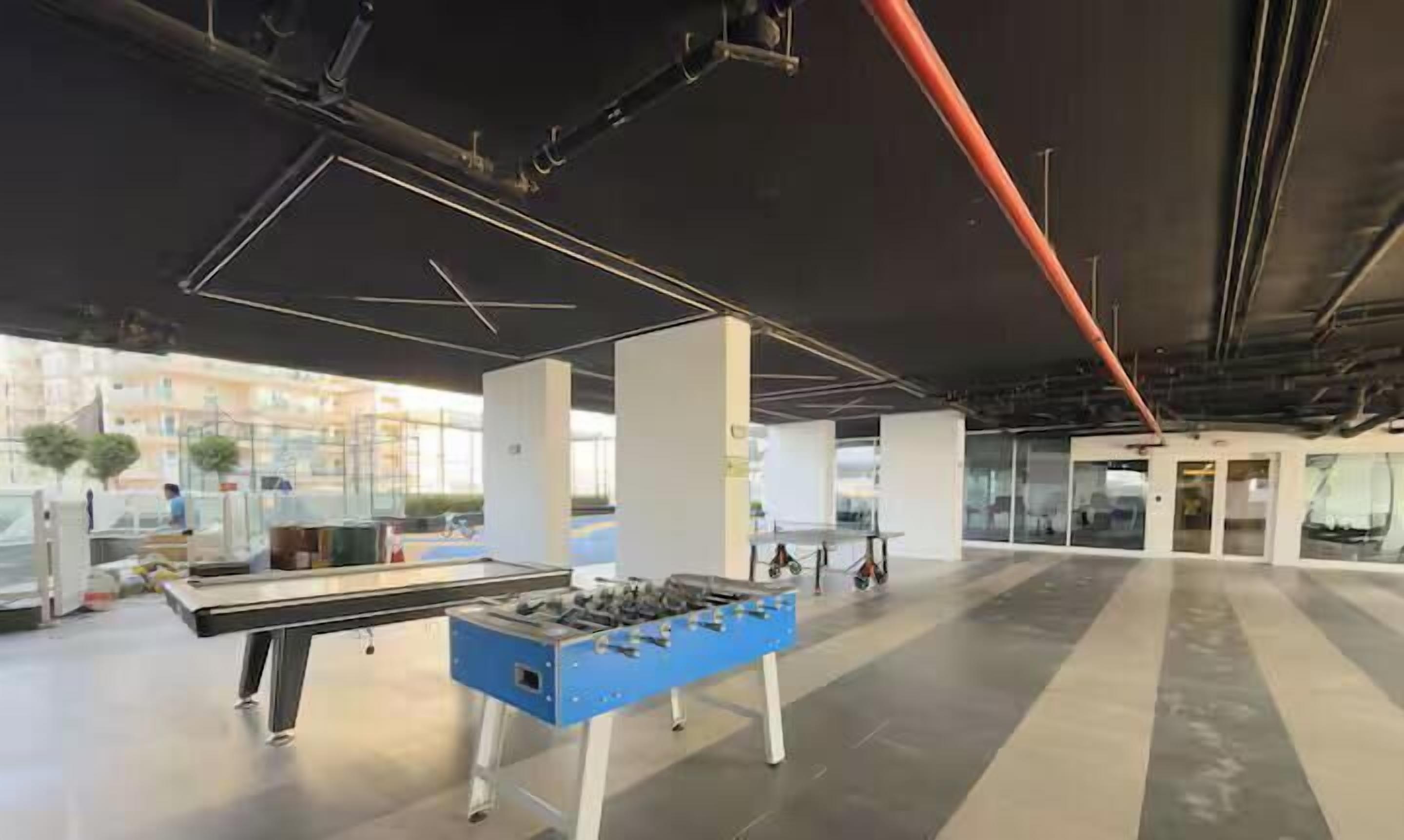 An indoor space with a foosball table, large windows, and a modern ceiling design.