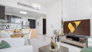 A modern living room with a flat-screen TV, a coffee table with decorative items, and a dining area with a kitchen in the background.
