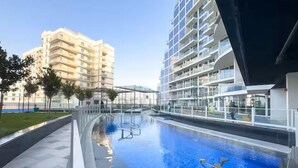 A modern swimming pool with clear water, surrounded by a glass enclosure, and adjacent to a high-rise building.