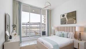 A modern bedroom with a large bed, a bedside table, a nightstand, a mirror, and a view of the outside.