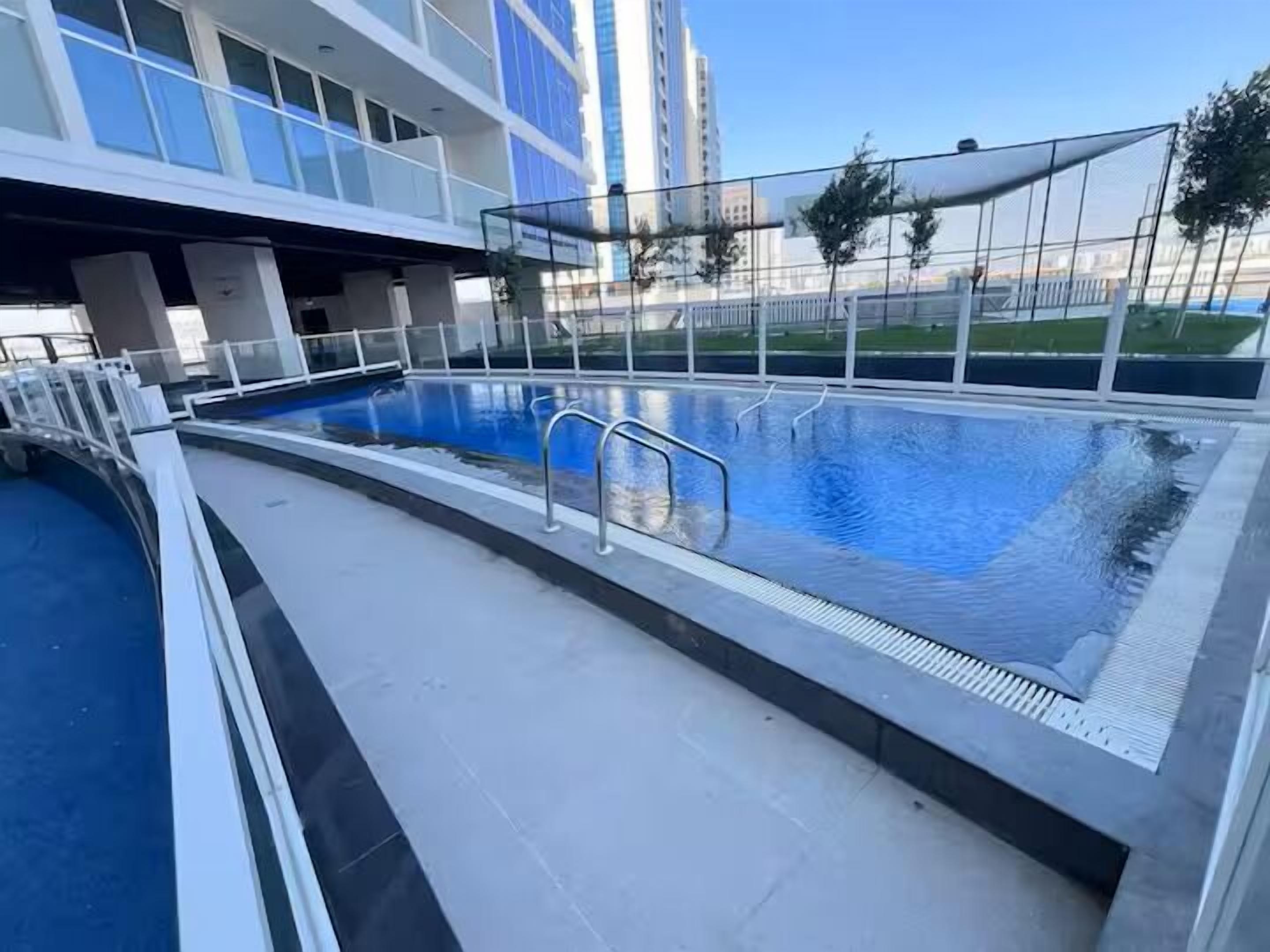 A swimming pool with a glass enclosure, surrounded by a white fence, and a building with large windows in the background.