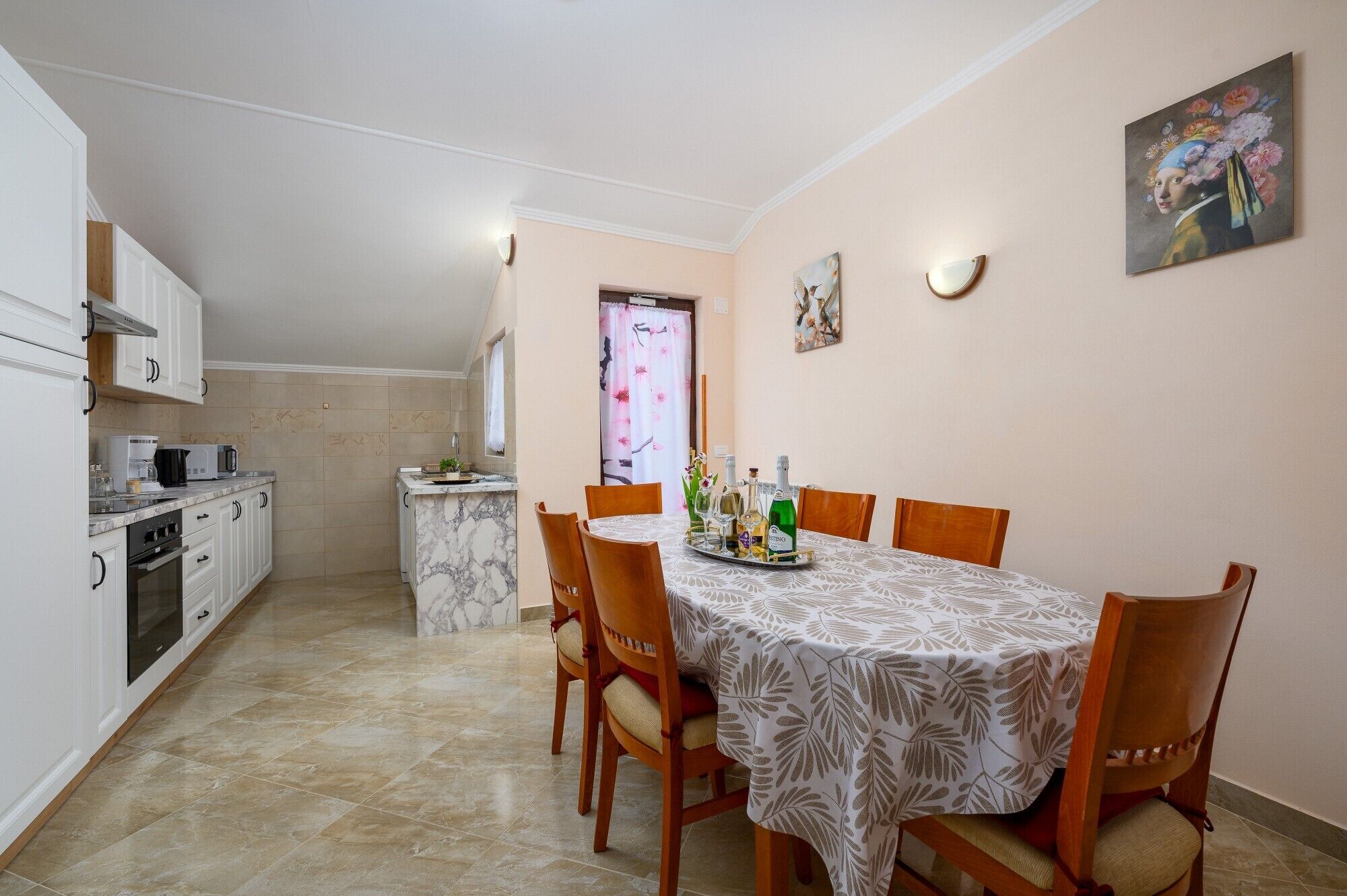 Cocina compacta con muebles blancos, encimera de mármol y comedor con mesa para cuatro.