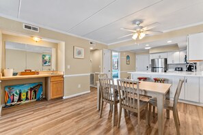 A modern kitchen with white cabinets, a dining area with wooden chairs, and a ceiling fan. - Oceanfront Condo with Pools and Beach Access (Nags Head)