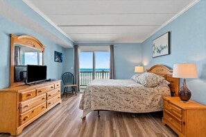A bedroom with a bed, a dresser, a television, a chair, and a view of the ocean. - Oceanfront Condo with Pools and Beach Access (Nags Head)